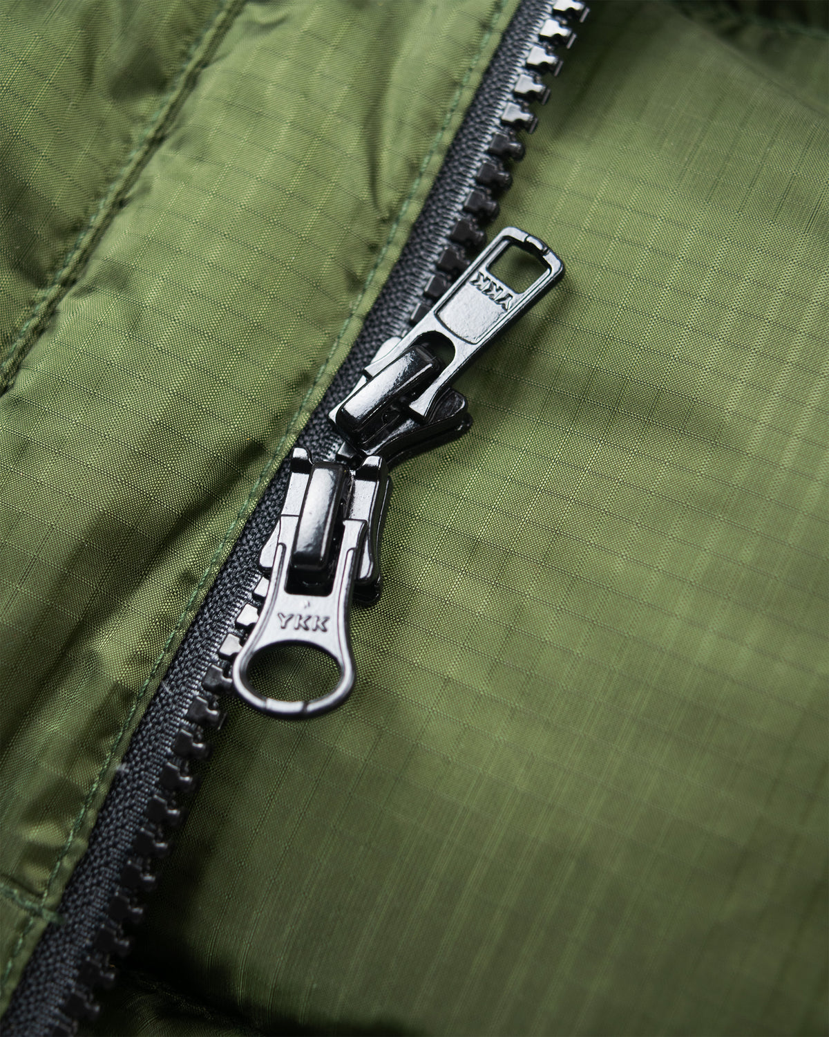 Black YKK zipper with metallic pull tab on green ripstop nylon down sweater quilted fabric