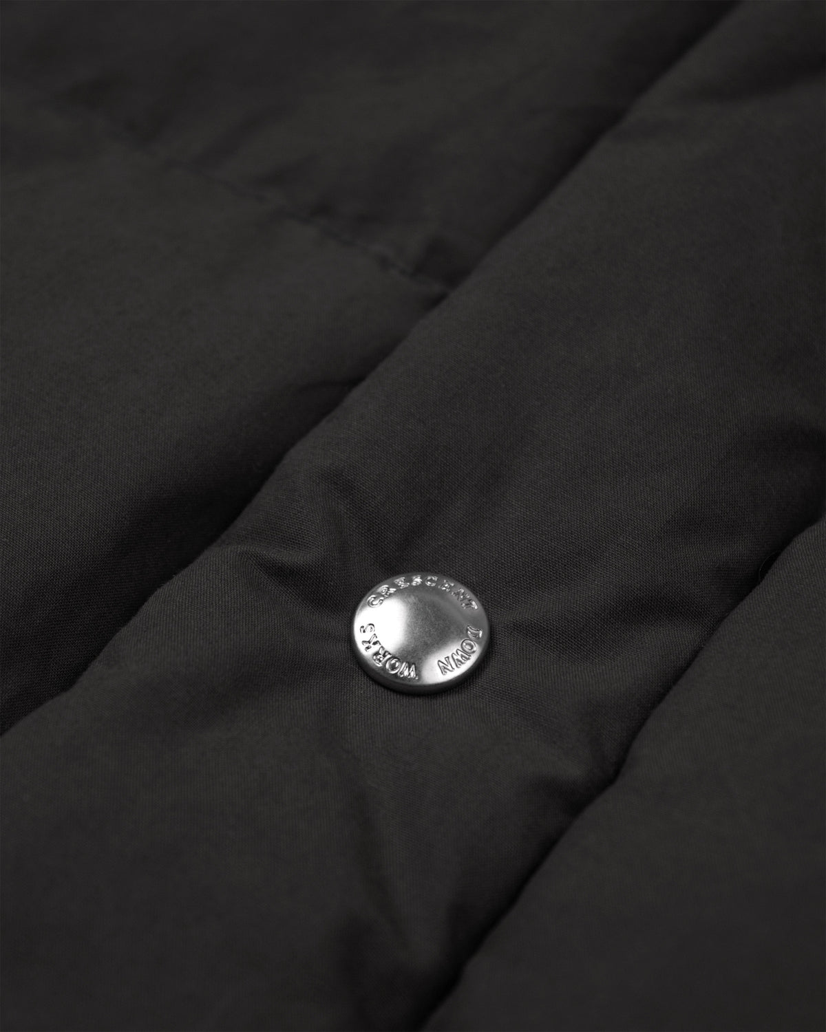 Silver circular button with engraved text on black quilted dry wax cotton fabric of down sweater