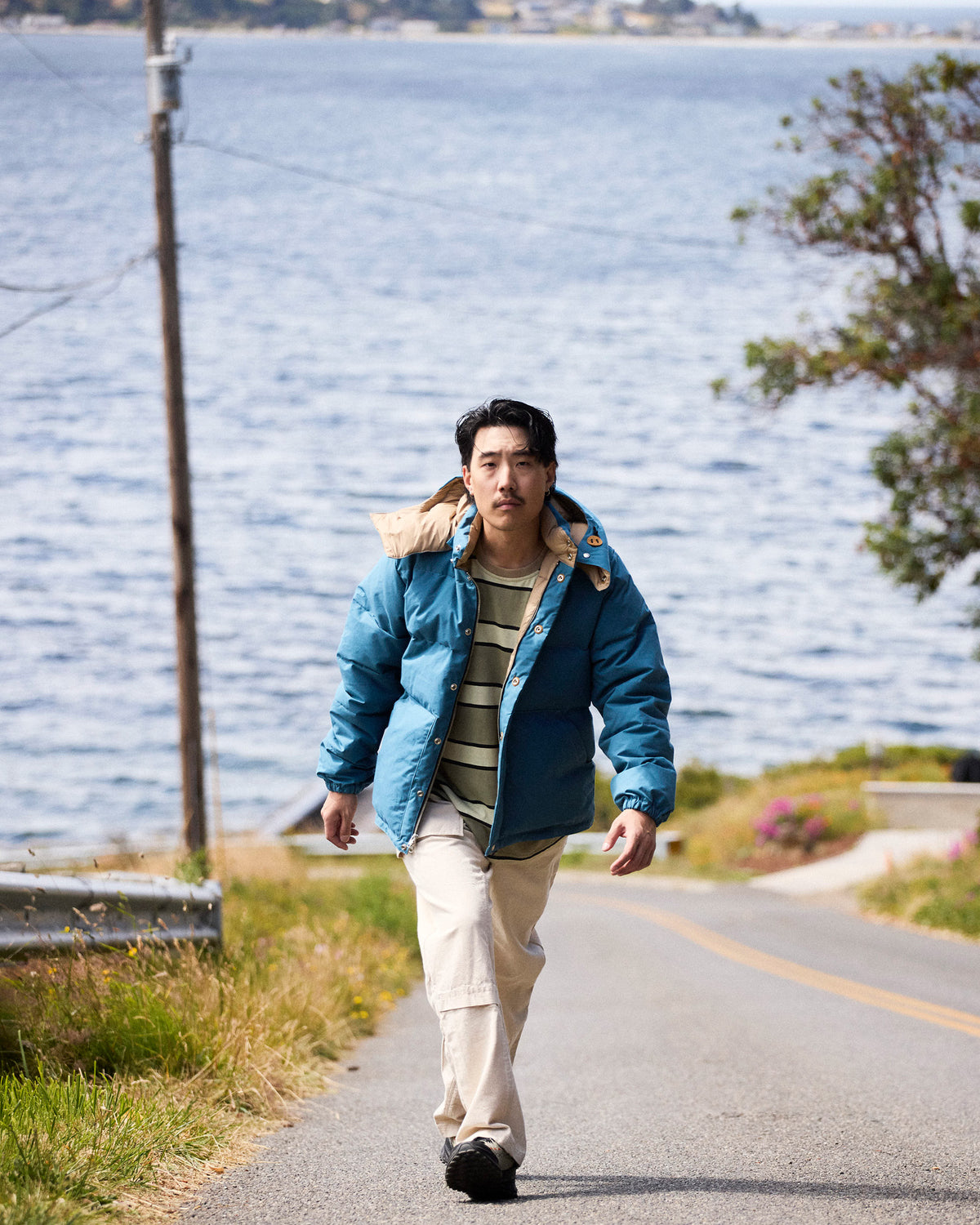 A man wearing a robin's blue down sweater in dry wax cotton with a beige-lined hood and matching cuffs layered over a striped shirt