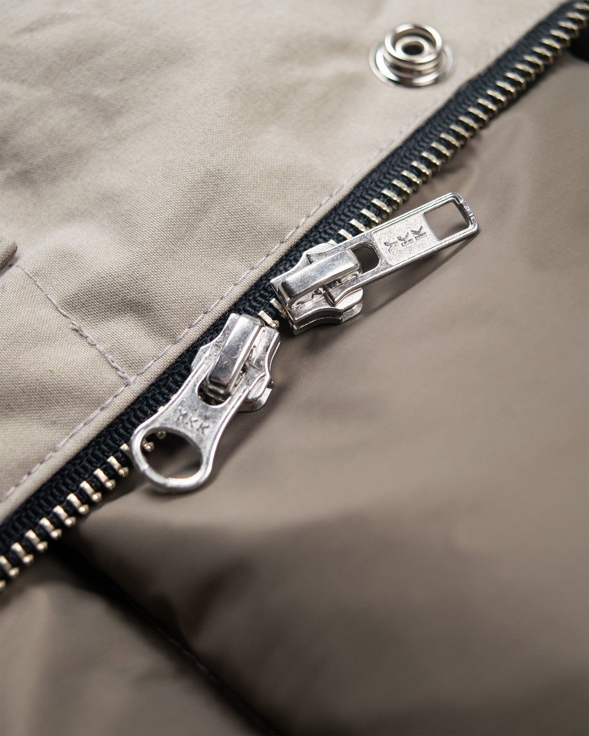 Silver metal zipper with black teeth on dry wax cotton fabric of down sweater stone color