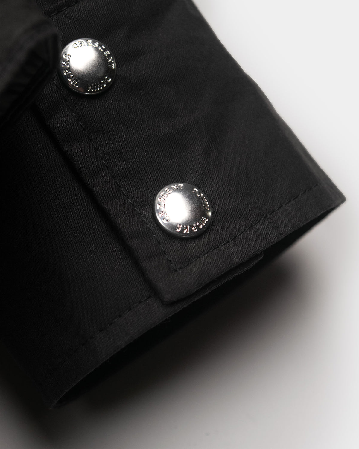 Black down shirt cuff made of dry wax cotton with two silver-toned engraved button fastenings