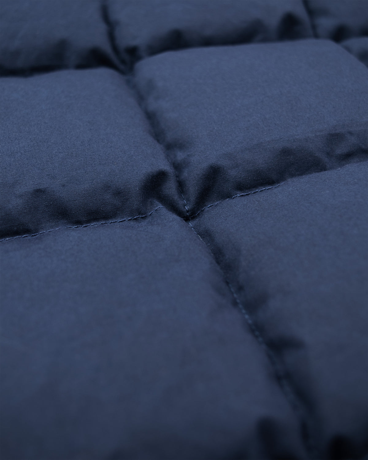 Close-up of a dark navy blue down chore coat fabric, showing stitched square sections and a soft texture.