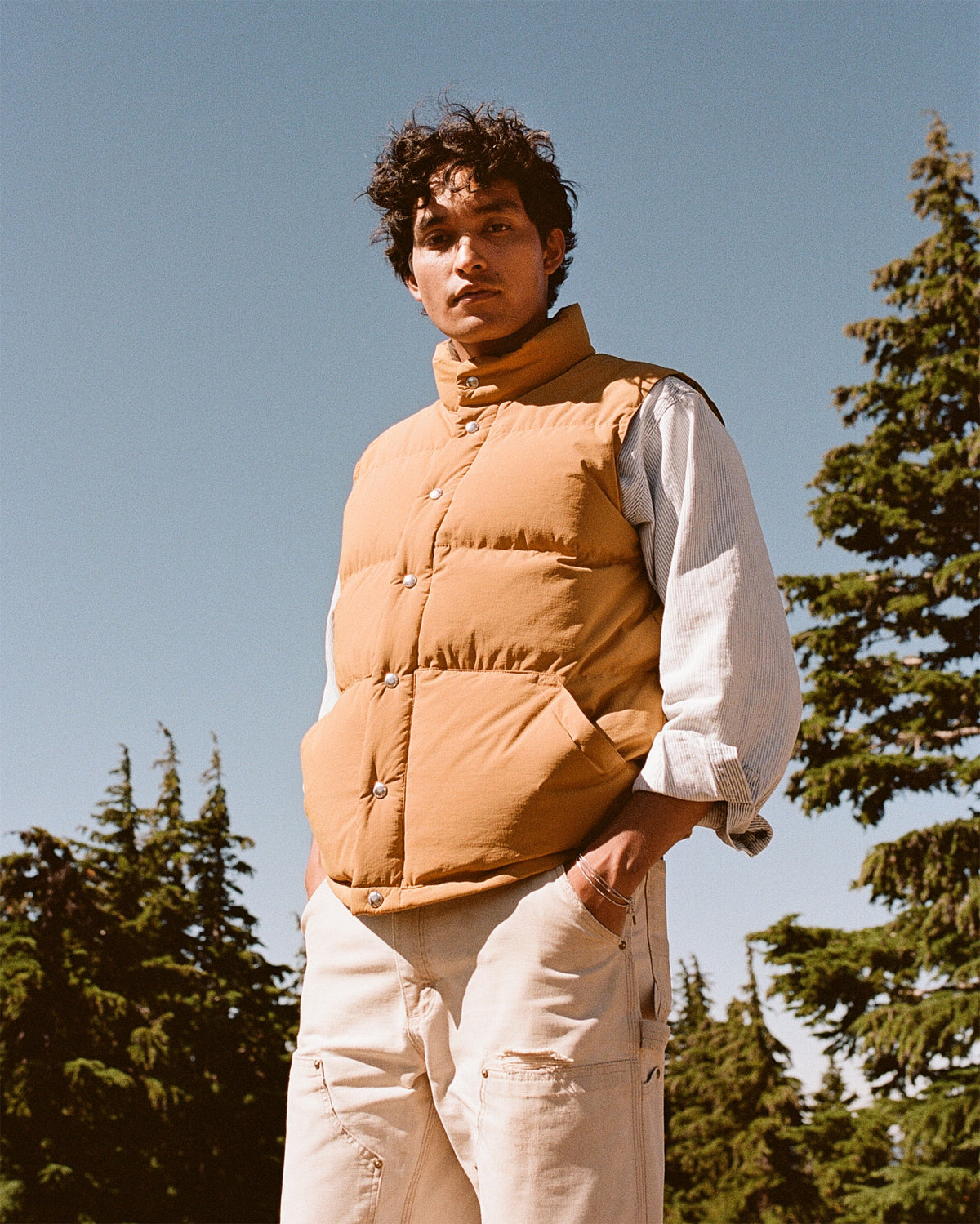 Person wearing a tan puffer vest with trees in the background