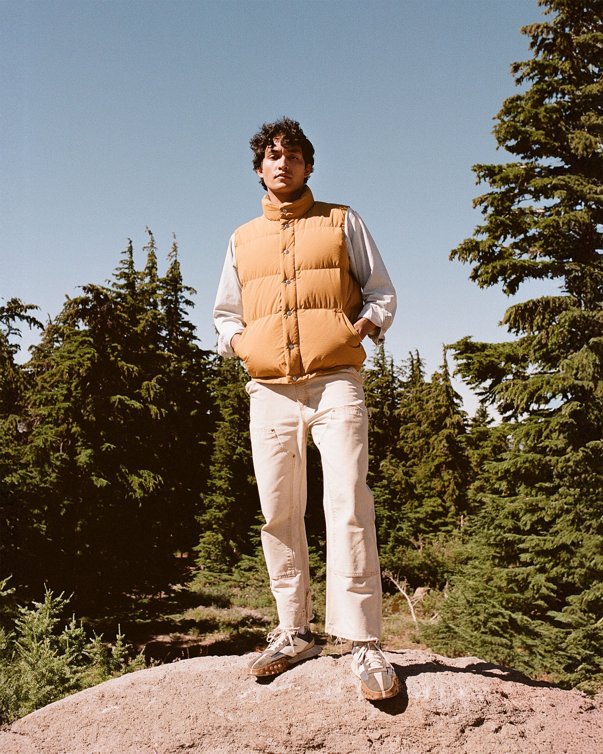 Person wearing a yellow puffer vest standing on a rock with trees in the background