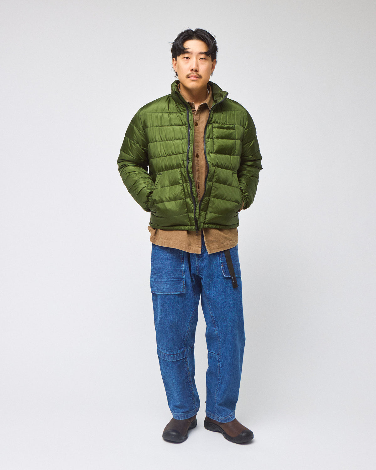 A model wearing a green Seattle Liner jacket with horizontal quilting, against a light gray background.