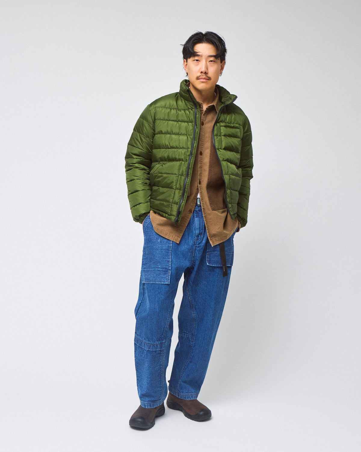 A model wearing a green Seattle Liner jacket with horizontal quilting, against a light gray background.