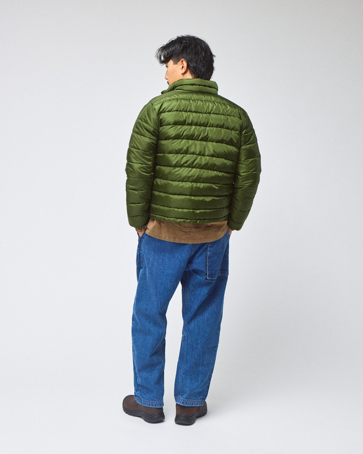 A model wearing a green Seattle Liner jacket with horizontal quilting, against a light gray background.