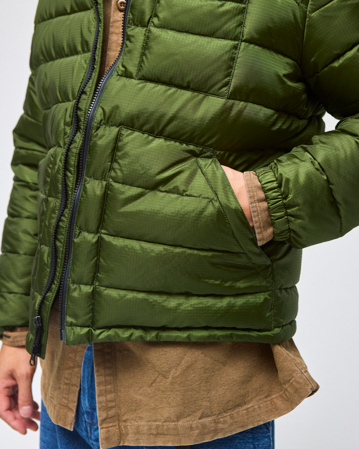 A closeup of model wearing a green Seattle Liner jacket with horizontal quilting, against a light gray background.