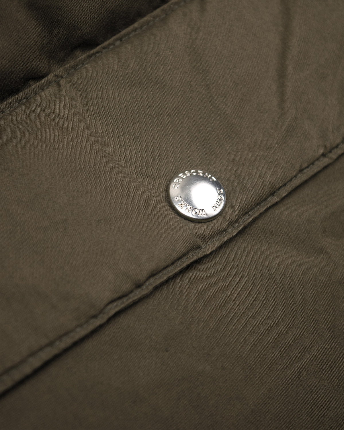 Silver circular button with engraved text on tent green dry waxed cotton fabric of classico down parka 