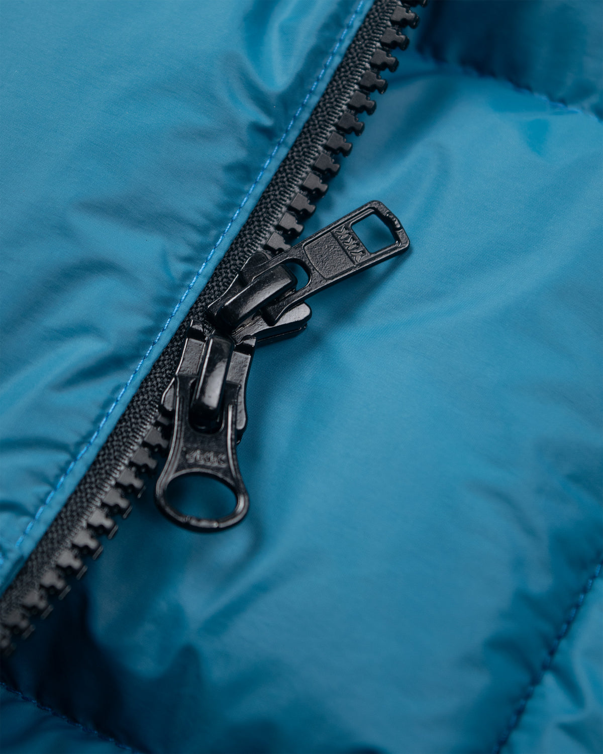 Black metal zipper with sturdy pull tab on duck blue nylon hooded sweatshirt puffer jacket fabric close up