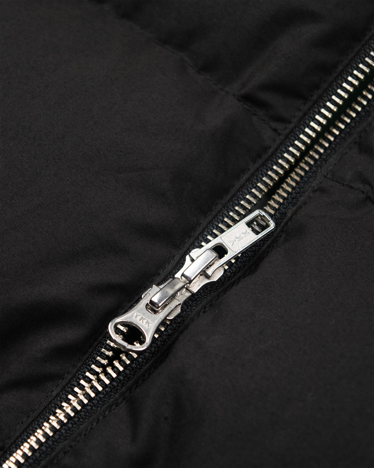 Black hooded sweatshirt in dry wax cotton featuring a close-up of a black puffer jacket zipper with silver metal pull tab