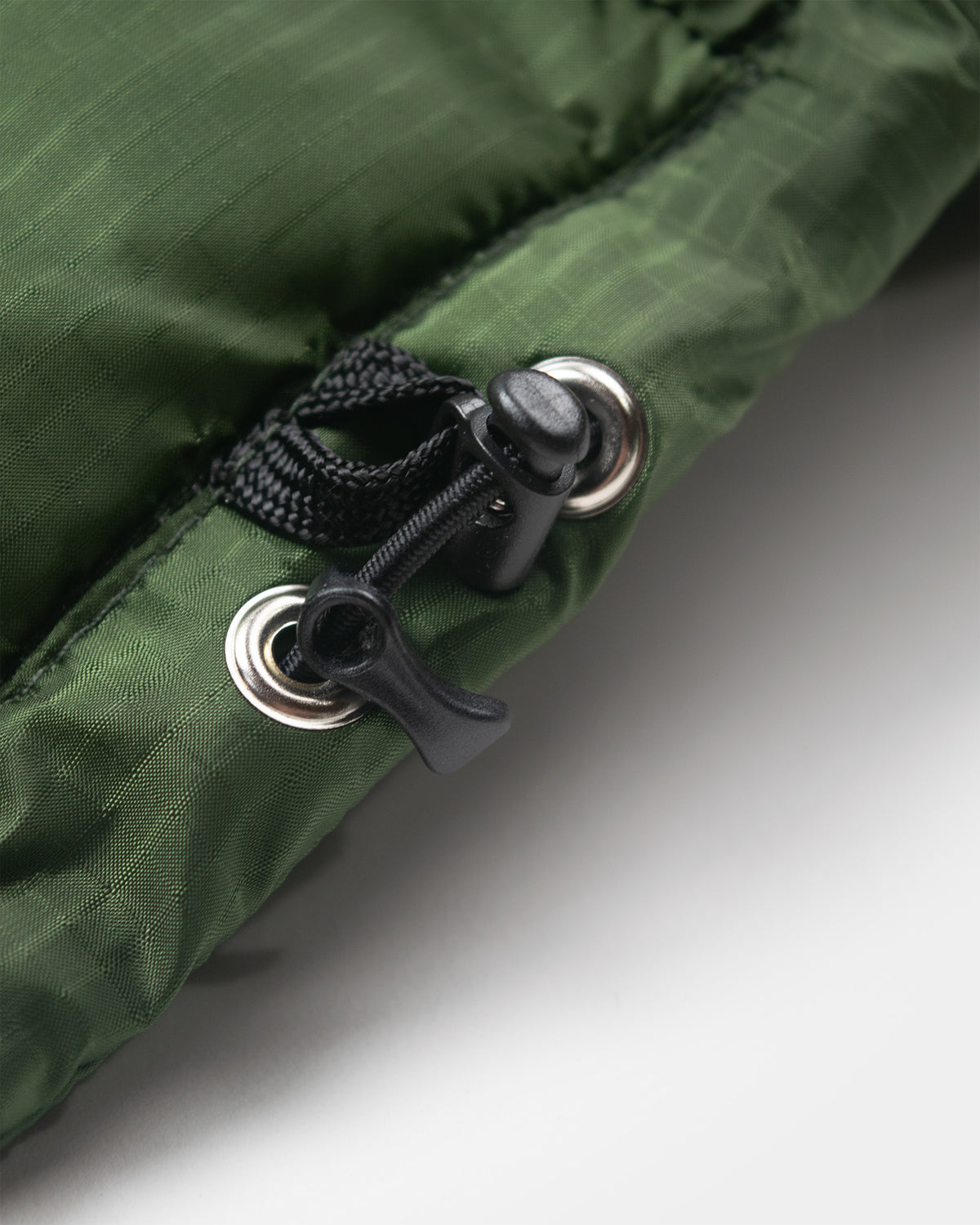 A detail closeup of the hem of a green Seattle Liner jacket against a light gray background.