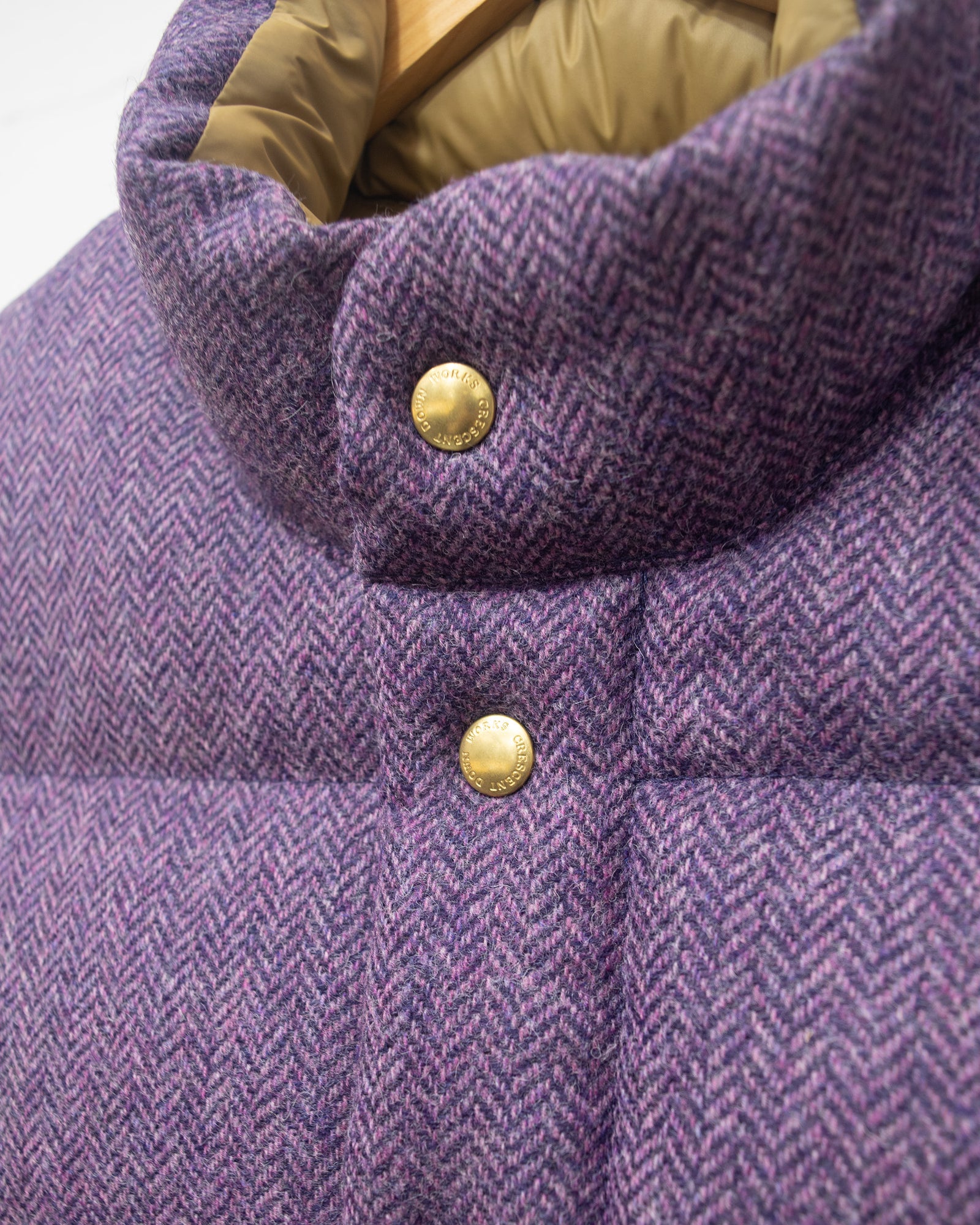A purple quilted puffer vest with  brass tone snap buttons, hanging on a wooden hanger on a clothing rack.