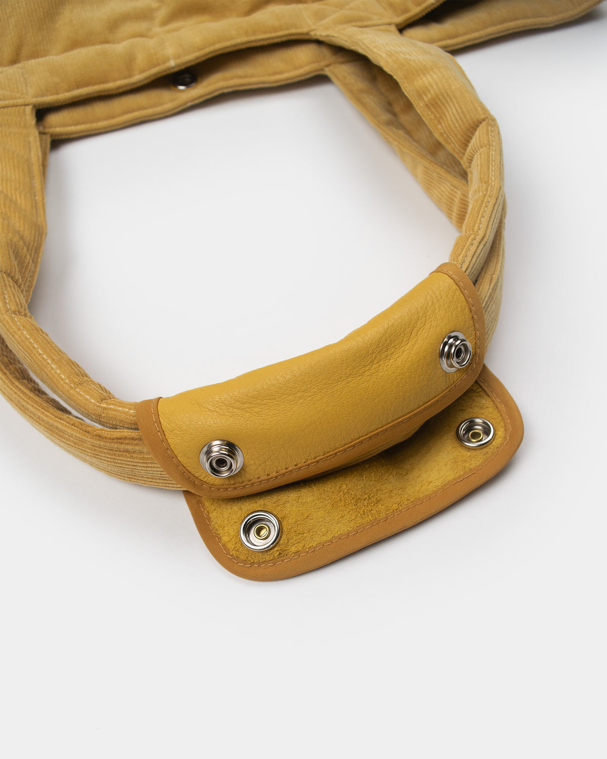 Close-up of a corduroy "corn" yellow corduroy down tote handle showing the leather handle open.