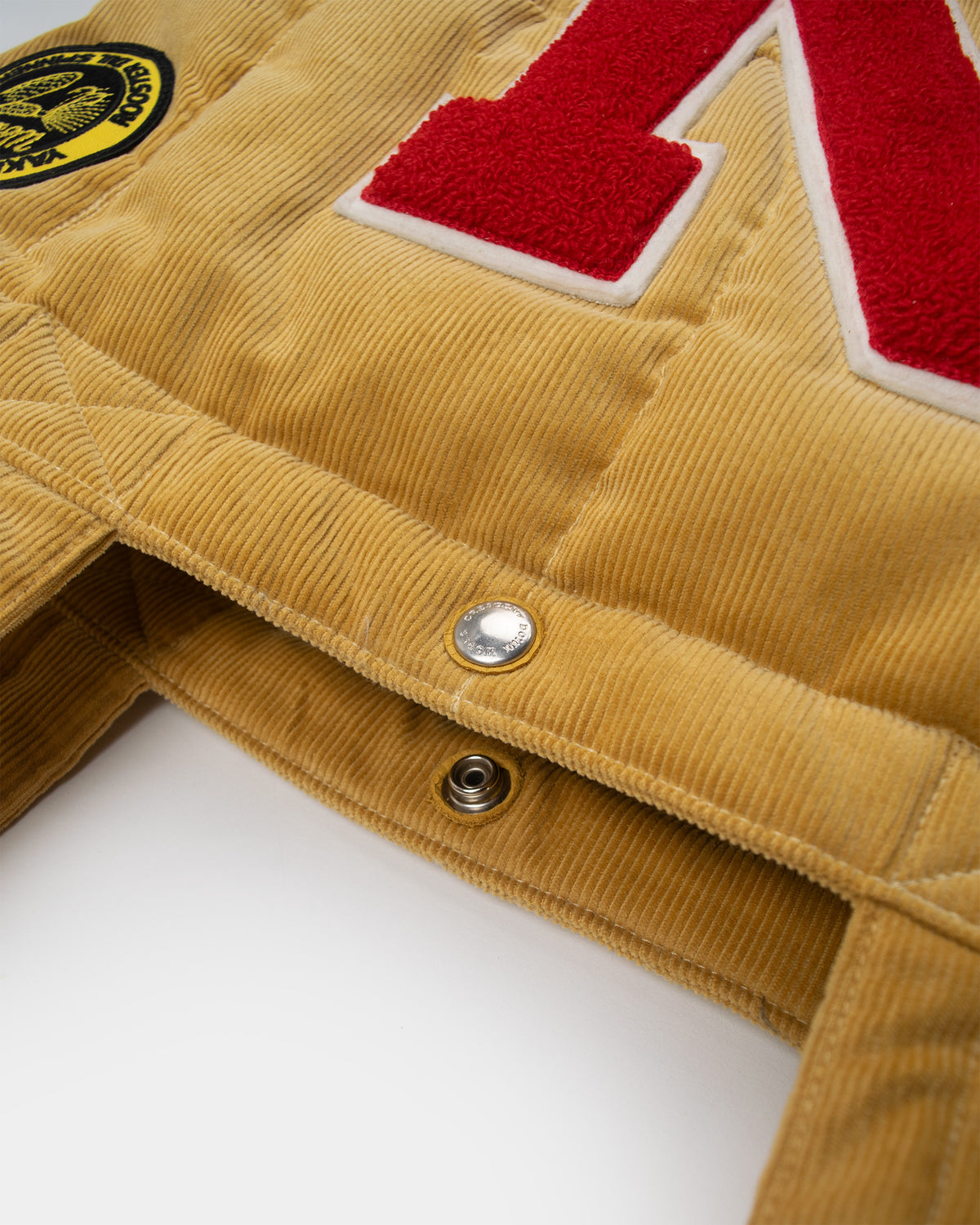 Close-up of a corduroy "corn" yellow corduroy down tote with a red and white embroidered letter 'N' on the front. 