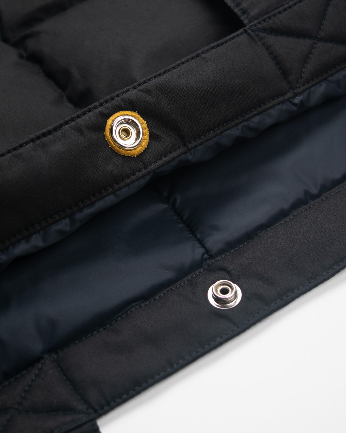 Black quilted down tote in dry wax cotton with leather snap reinforcement and silver metal grommet