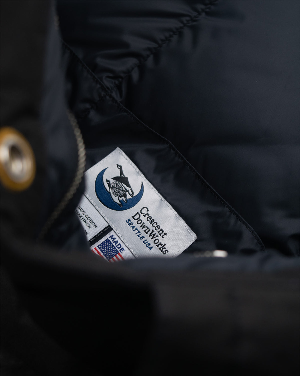 White rectangular label with black text and blue crescent moon logo on black dry wax cotton down tote by crescent downworks seattle usa