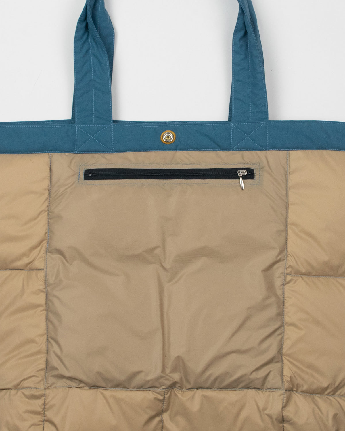A close-up of a puffer-style tote bag showing the inside panel in amber quilted fabric, a robin blue top band, two handles, a black horizontal zip pocket.