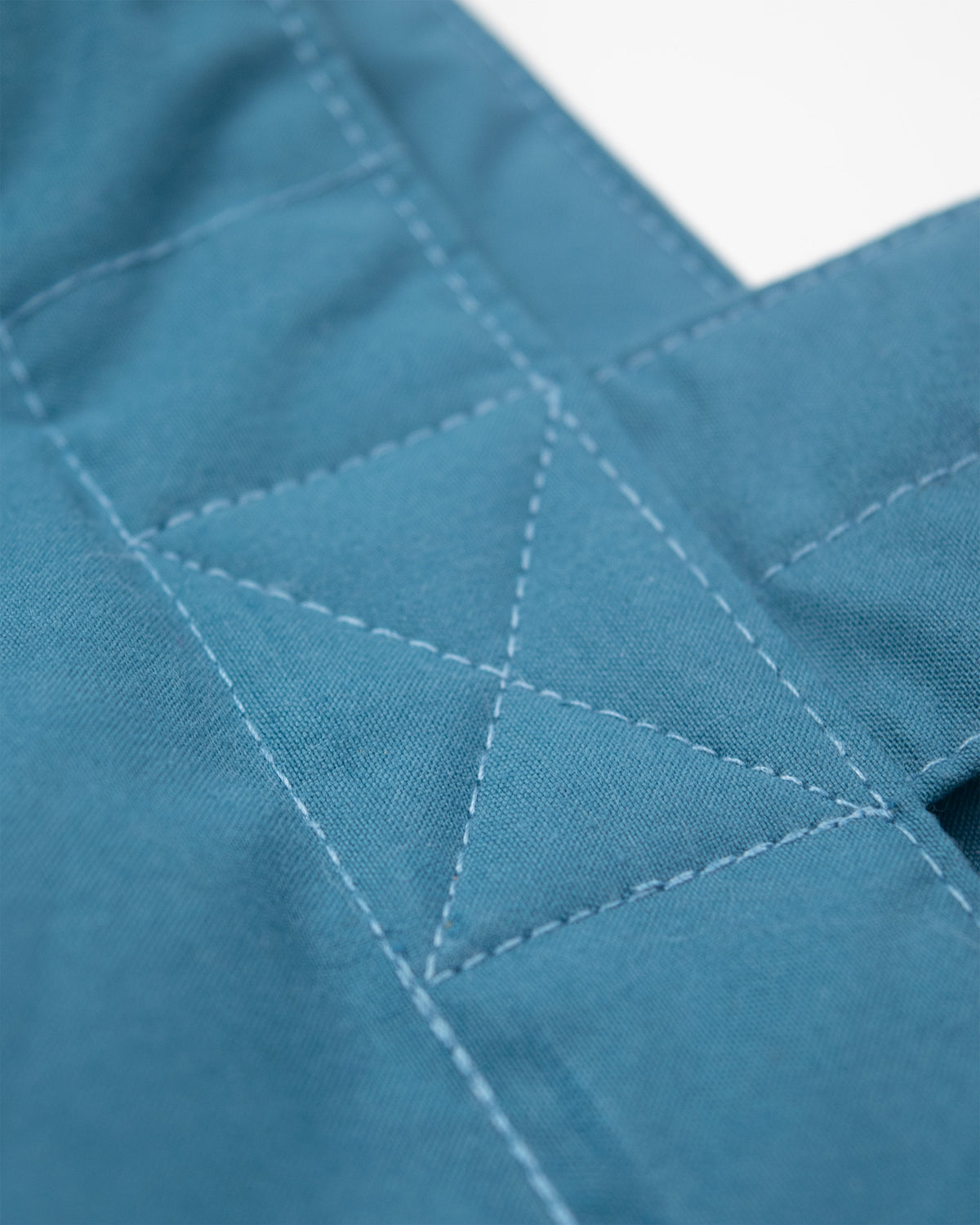 Close-up of a Robin Blue fabric tote bag showing a diamond-quilted pattern and part of a strap or folded edge against a white background.