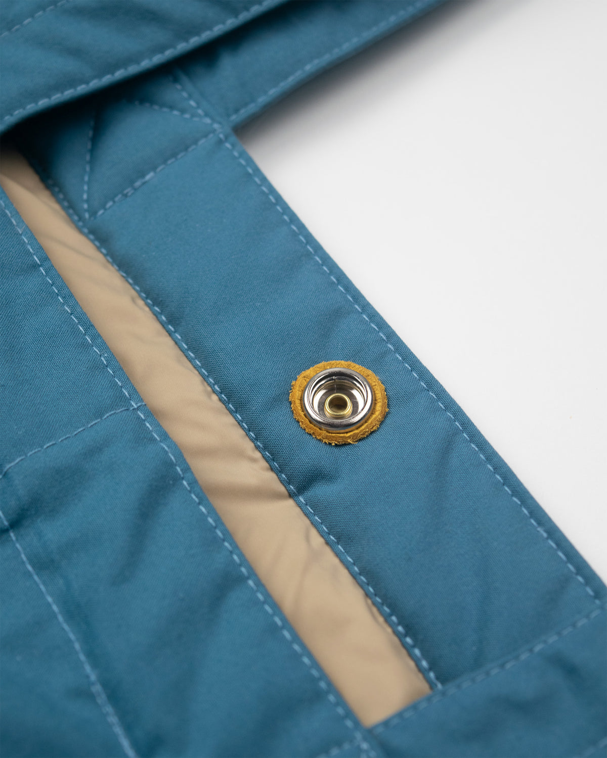 Close-up of a Robin Blue quilted Tote Bag with an amber inner lining and a metal snap button closure, reinforced with gold leather, set against a plain white background.